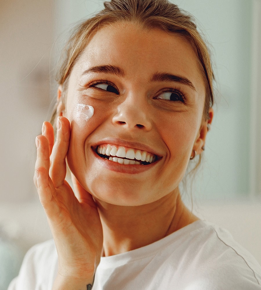 Woman applying cream and smiling at camera.