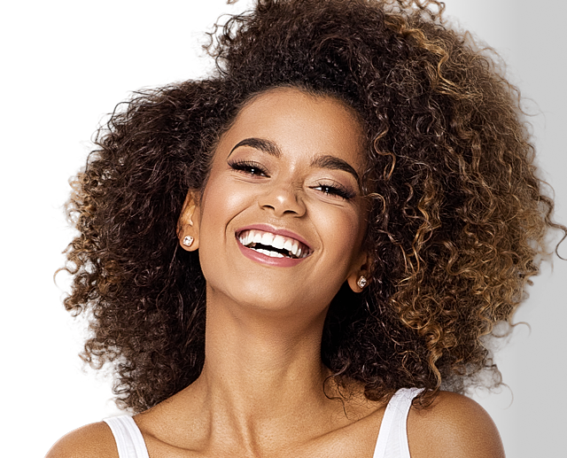 Smiling woman with curly hair against black background.
